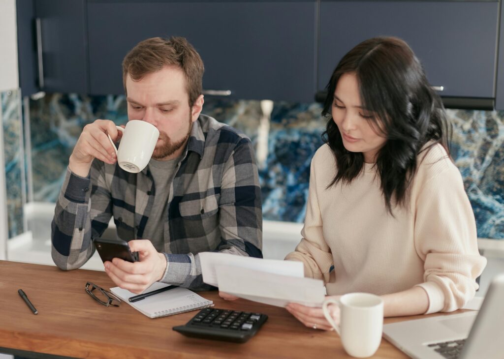 A couple reviewing bills, using a calculator and smartphone, in a modern kitchen.